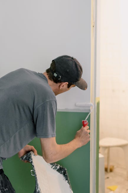 Back view of unrecognizable male in cap holding roller while painting walls in room